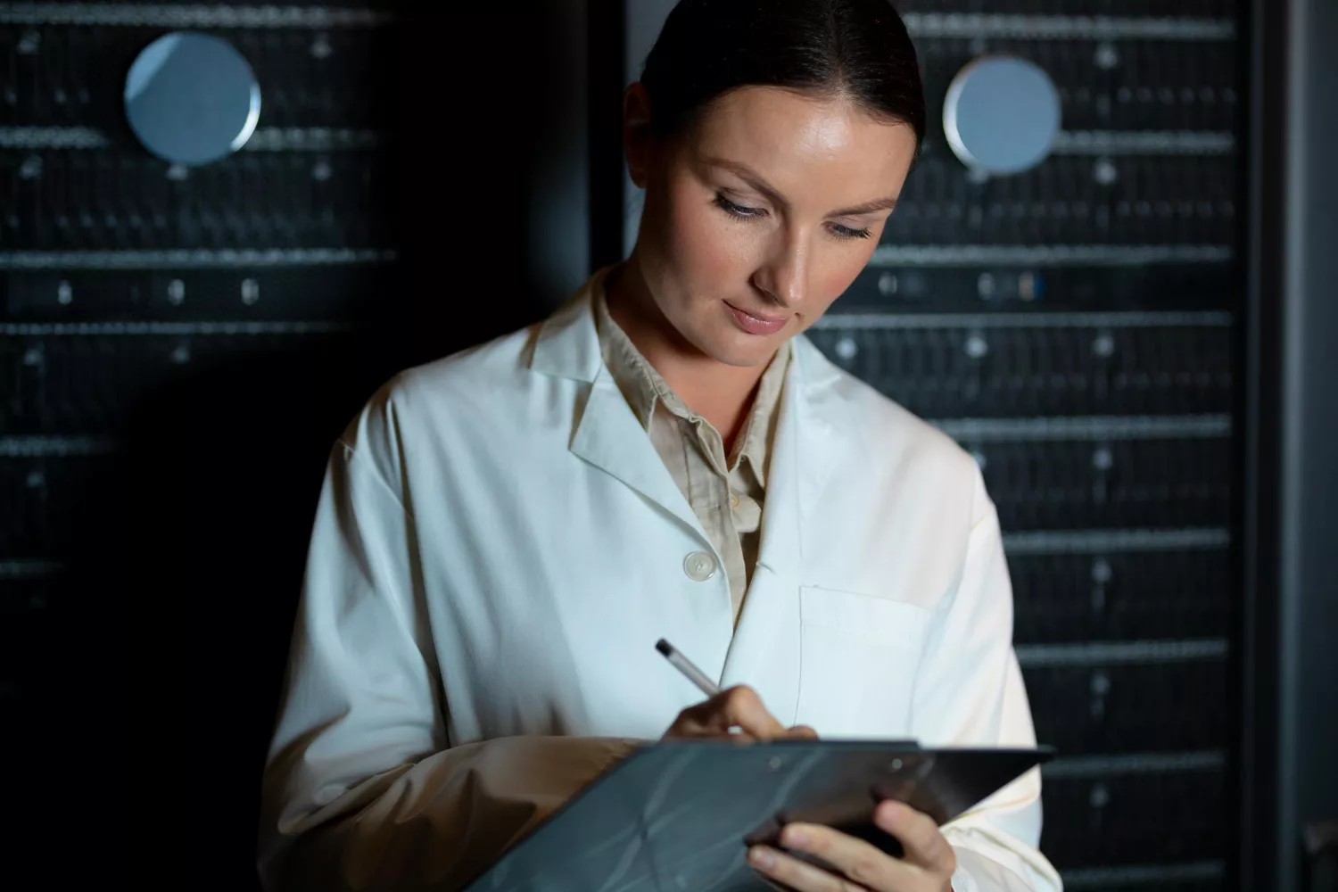 A woman in a lab coat reviews a clipboard in a server room, illustrating cyber background checks in action.