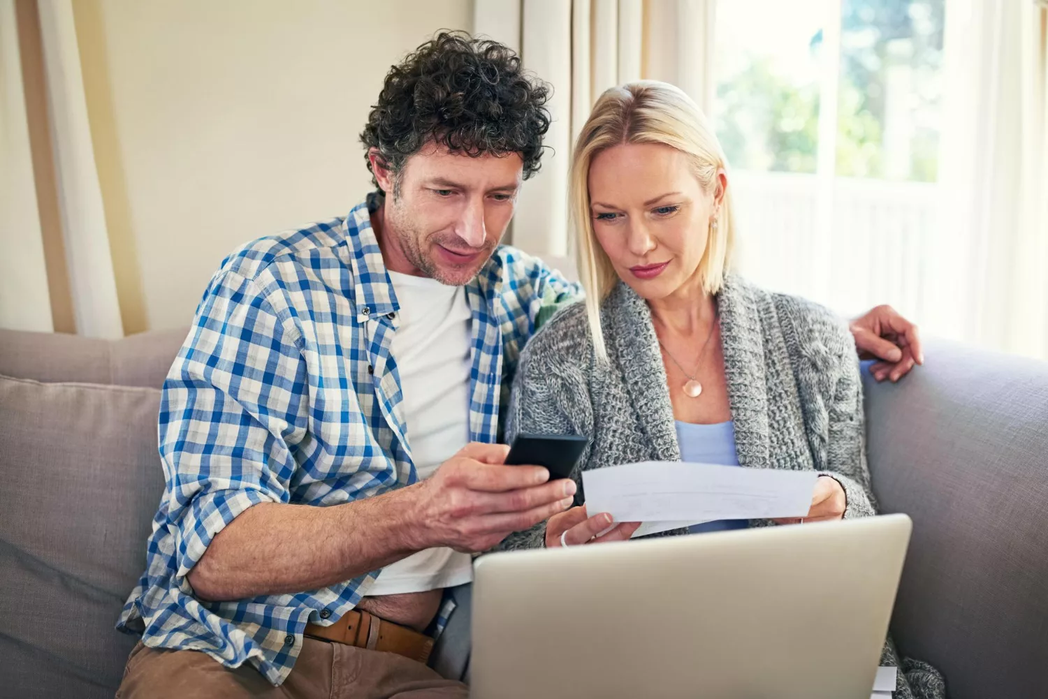 A couple sitting together looking at their phone with a laptop infront of them