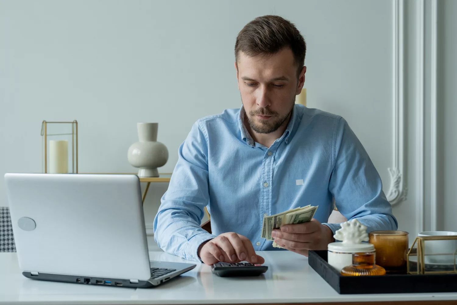 Man calculating cyber liability insurance cost at desk with laptop and cash.