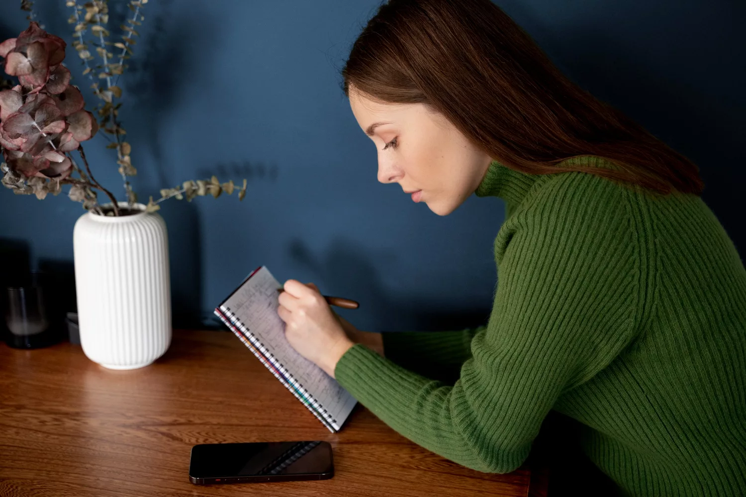 A woman in a green sweater takes notes on business insurance requirements for startups at a wooden table.