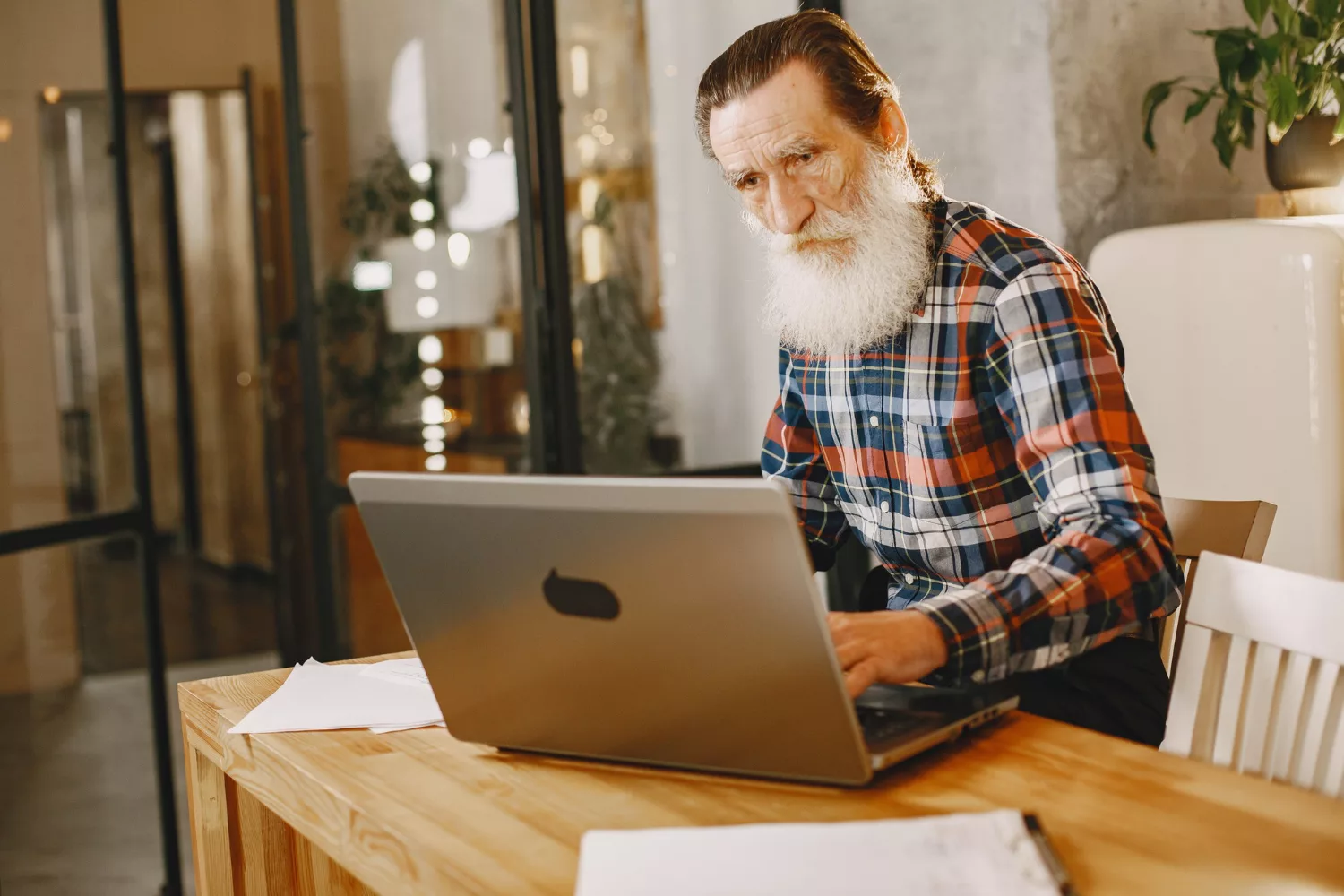 Older man working on a laptop at a wooden table in a home office, representing best hosting for small business research and website management.